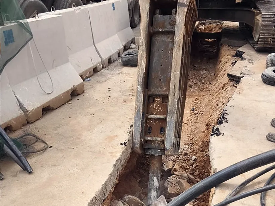 Hydraulic breaker cutting rock in a trench